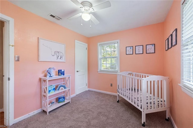 carpeted bedroom with a ceiling fan, visible vents, a nursery area, and baseboards