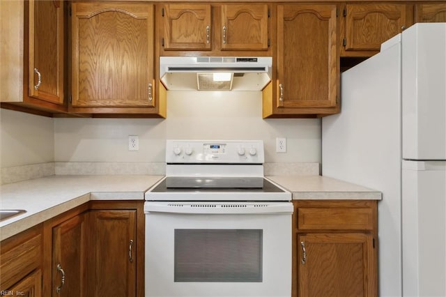 kitchen with white appliances, under cabinet range hood, light countertops, and brown cabinetry