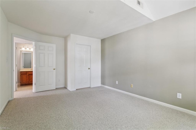 unfurnished bedroom with light carpet, baseboards, and ensuite bath