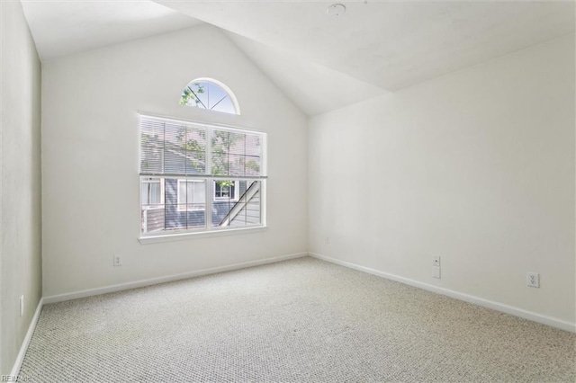 carpeted empty room featuring vaulted ceiling and baseboards