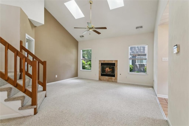 unfurnished living room with light carpet, a skylight, stairs, high vaulted ceiling, and a fireplace