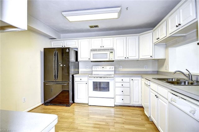 kitchen with light wood-style flooring, a sink, white cabinetry, and white appliances