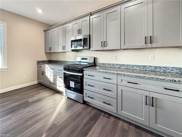 kitchen with appliances with stainless steel finishes, gray cabinetry, dark wood-style flooring, recessed lighting, and light stone countertops