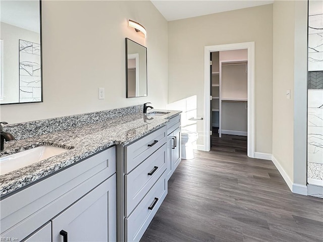 bathroom featuring double vanity, a tile shower, baseboards, and a sink