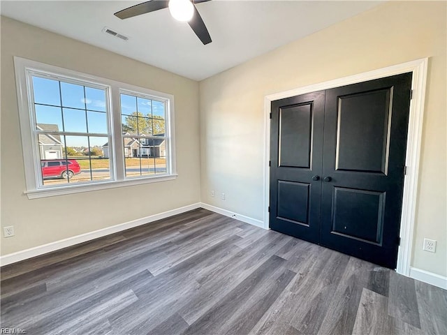 unfurnished bedroom featuring a closet, a ceiling fan, visible vents, baseboards, and wood finished floors