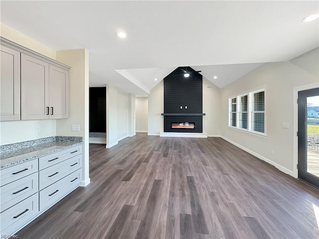 unfurnished living room with a large fireplace, baseboards, vaulted ceiling, and dark wood finished floors