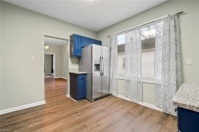kitchen with light wood-type flooring, baseboards, blue cabinets, and stainless steel fridge with ice dispenser
