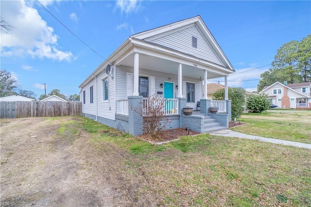shotgun-style home with fence, covered porch, and a front lawn