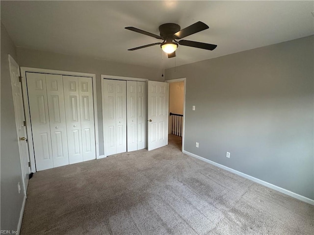 unfurnished bedroom with baseboards, a ceiling fan, carpet, and two closets