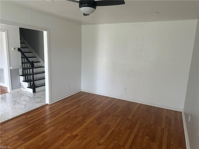 spare room with ceiling fan, stairs, visible vents, baseboards, and wood finished floors