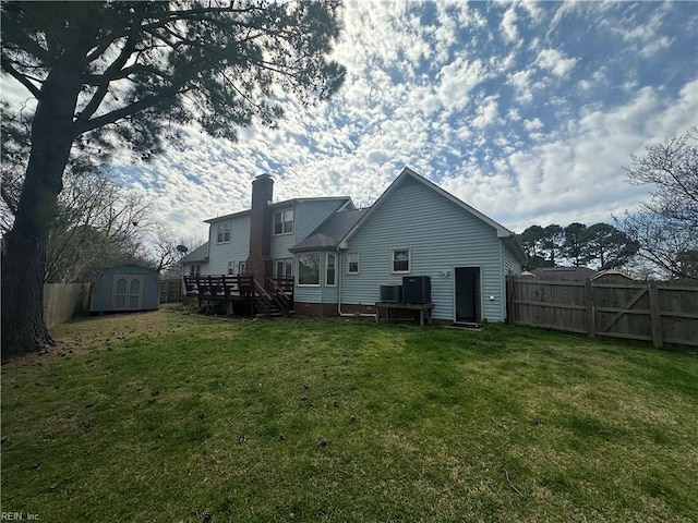 back of house featuring a wooden deck, a chimney, an outbuilding, a storage shed, and fence