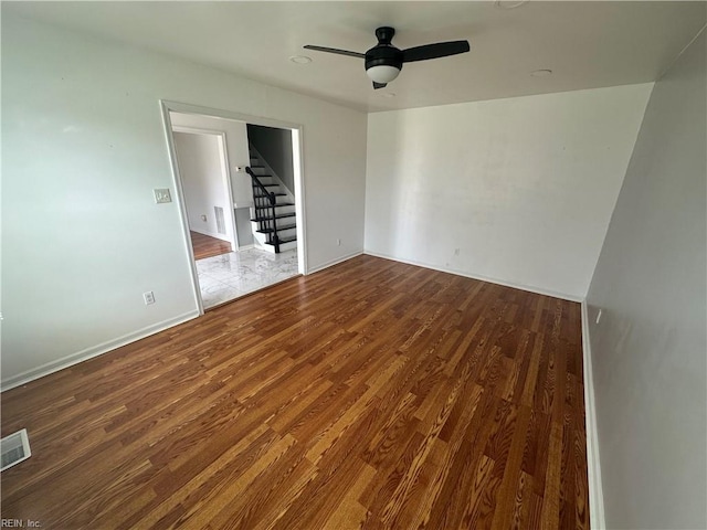 empty room featuring stairway, ceiling fan, visible vents, baseboards, and wood finished floors