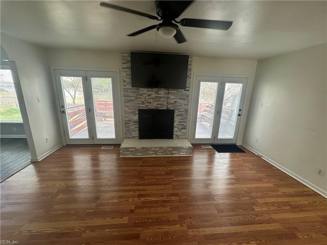 unfurnished living room featuring a ceiling fan, baseboards, wood finished floors, and a fireplace