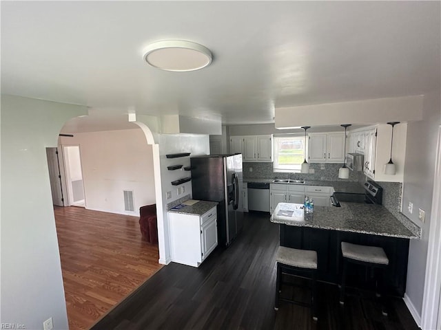 kitchen with dark wood finished floors, arched walkways, appliances with stainless steel finishes, a sink, and a peninsula