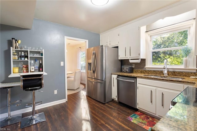 kitchen featuring appliances with stainless steel finishes, light stone countertops, dark wood finished floors, a sink, and white cabinets