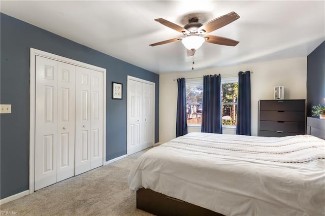 carpeted bedroom with baseboards, ceiling fan, and two closets