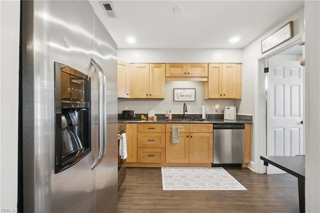 kitchen featuring a sink, dark countertops, light brown cabinets, stainless steel appliances, and dark wood finished floors
