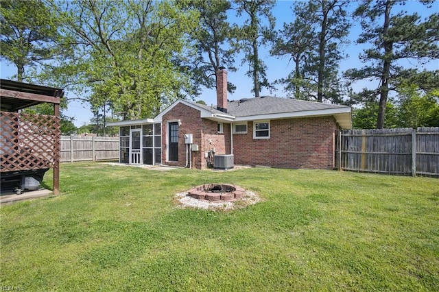 rear view of property with a sunroom, central AC unit, a fenced backyard, brick siding, and a fire pit