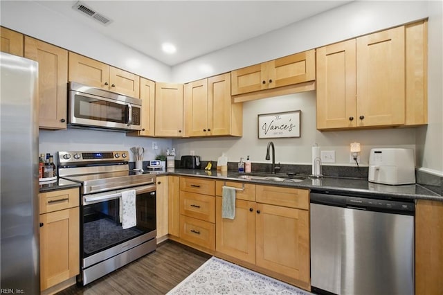 kitchen with dark countertops, light brown cabinets, appliances with stainless steel finishes, and a sink