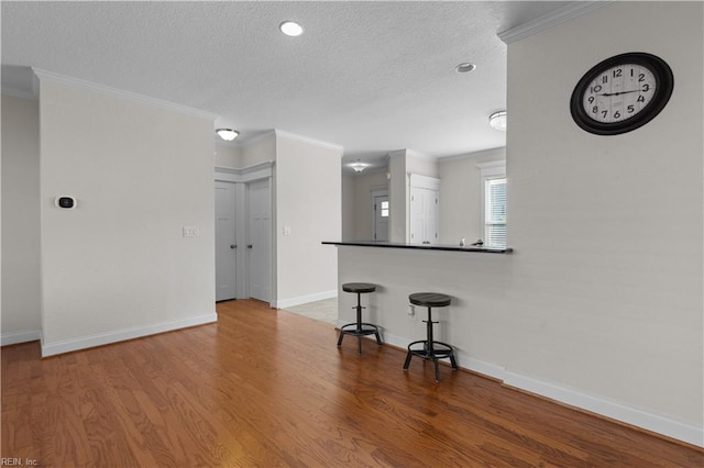 unfurnished living room featuring baseboards, a textured ceiling, ornamental molding, and wood finished floors