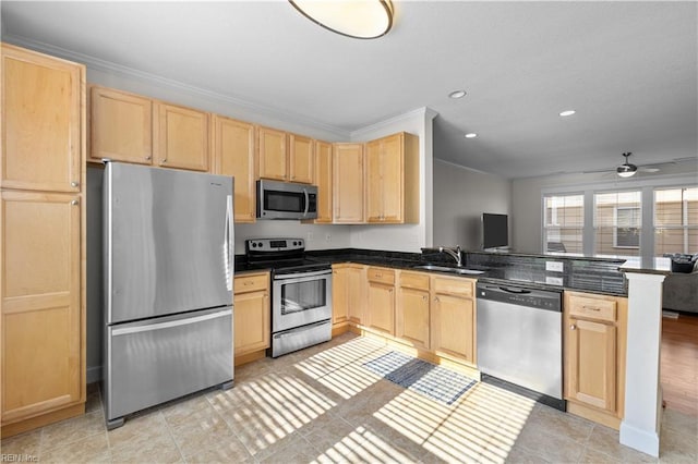 kitchen featuring appliances with stainless steel finishes, dark countertops, light brown cabinetry, a sink, and a peninsula
