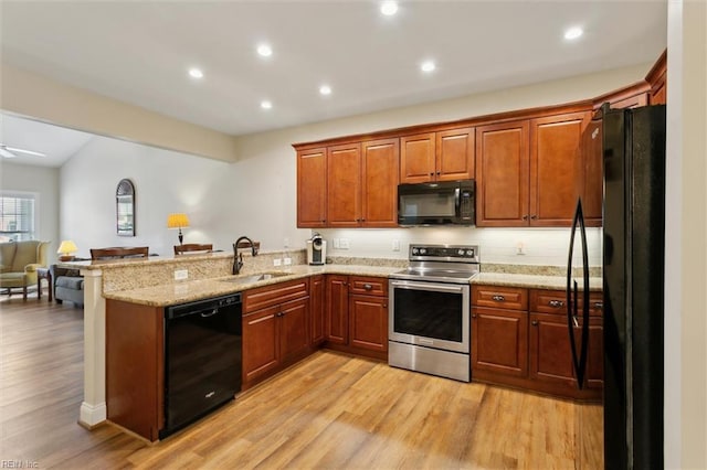 kitchen featuring a sink, black appliances, a peninsula, open floor plan, and light wood-style flooring