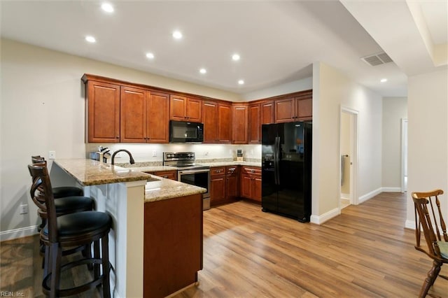 kitchen featuring light stone counters, a sink, a peninsula, recessed lighting, and black appliances
