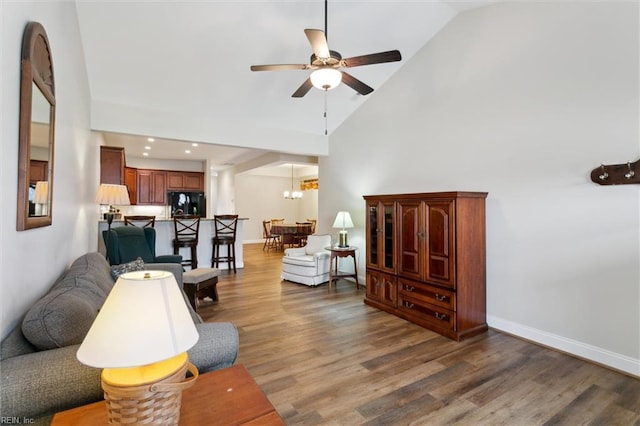 living area with baseboards, ceiling fan with notable chandelier, wood finished floors, and high vaulted ceiling
