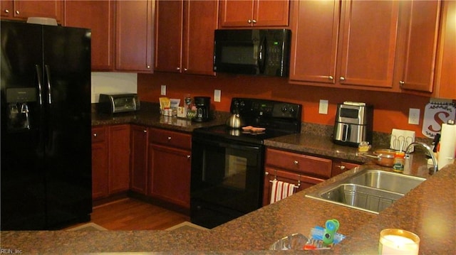 kitchen with black appliances, wood finished floors, dark countertops, and a sink