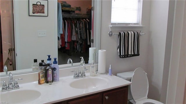 full bathroom featuring a spacious closet, toilet, double vanity, and a sink