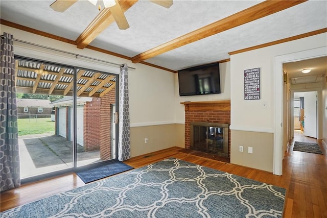 unfurnished living room featuring wood finished floors, beamed ceiling, ornamental molding, ceiling fan, and a fireplace