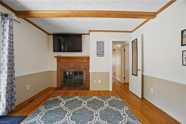 unfurnished living room with wood finished floors, beamed ceiling, a wainscoted wall, a fireplace, and visible vents