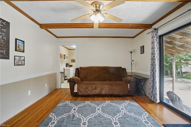sitting room with a ceiling fan, wood finished floors, a wainscoted wall, and beamed ceiling
