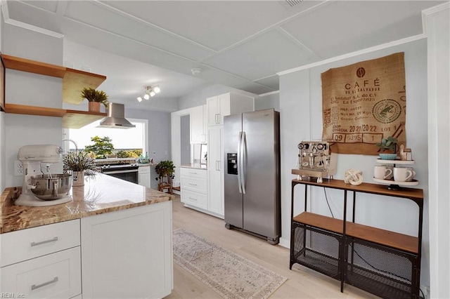 kitchen with wall chimney range hood, stainless steel appliances, light stone countertops, and white cabinetry