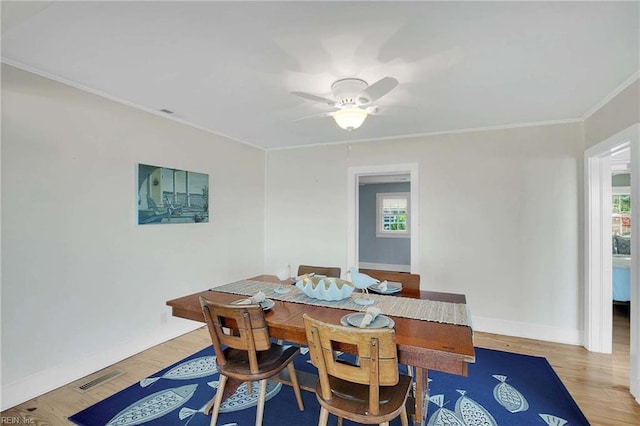 dining space with a ceiling fan, visible vents, wood finished floors, baseboards, and ornamental molding