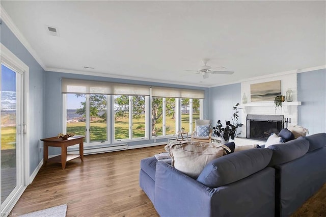 living area featuring ceiling fan, visible vents, a fireplace, a baseboard heating unit, and ornamental molding