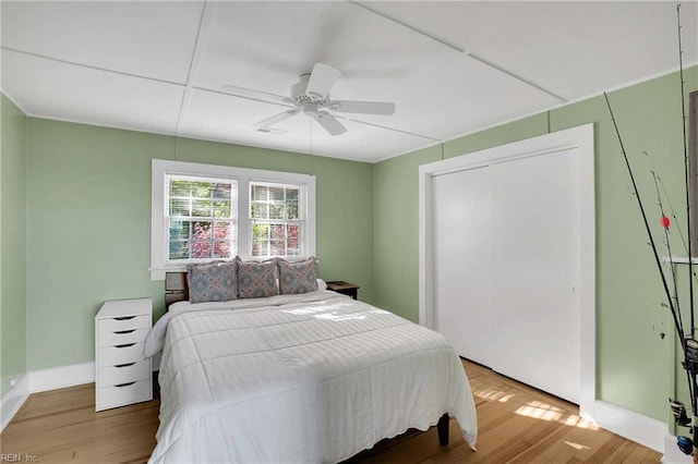 bedroom featuring visible vents, a closet, wood finished floors, baseboards, and a ceiling fan