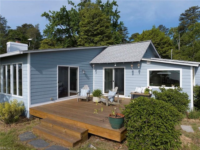 rear view of property with roof with shingles, a wooden deck, and a chimney