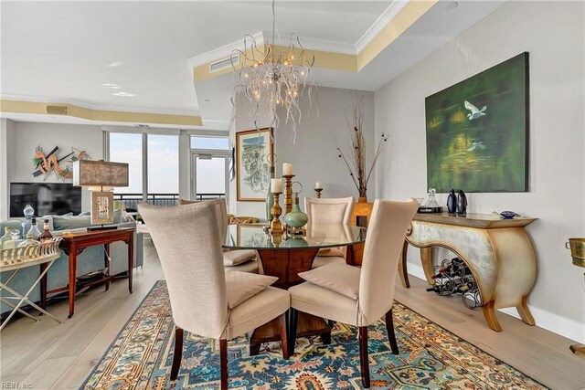 dining space with a tray ceiling, a chandelier, light wood-style flooring, and visible vents