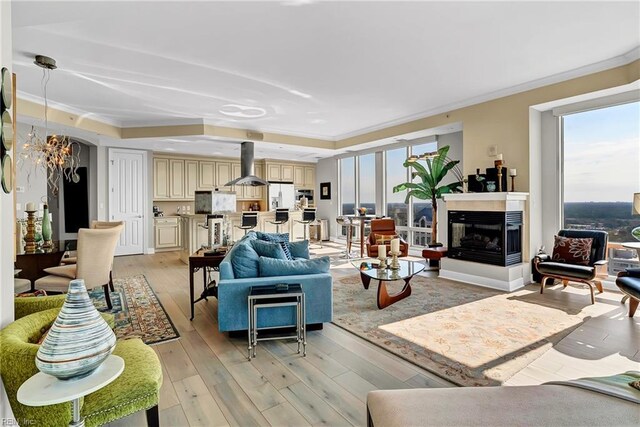 living room featuring a multi sided fireplace, a chandelier, ornamental molding, and light wood-style flooring