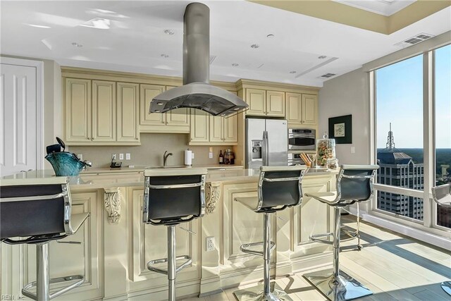 kitchen featuring cream cabinets, light countertops, stainless steel appliances, island range hood, and visible vents