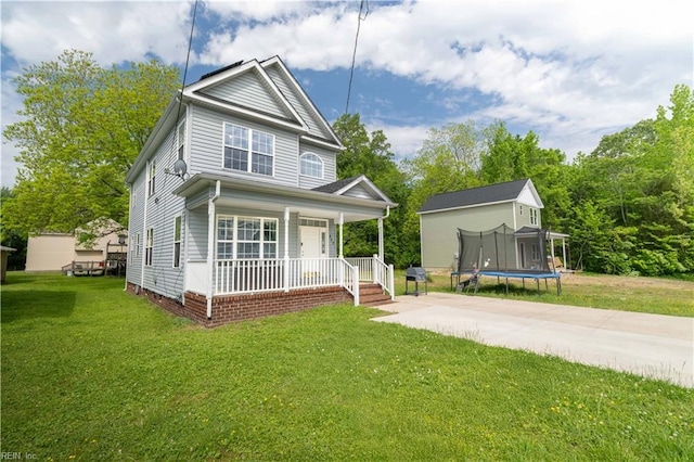 view of front of home with covered porch, a trampoline, and a front lawn