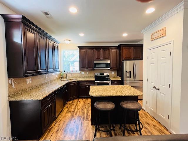 kitchen featuring appliances with stainless steel finishes, a sink, a center island, decorative backsplash, and visible vents