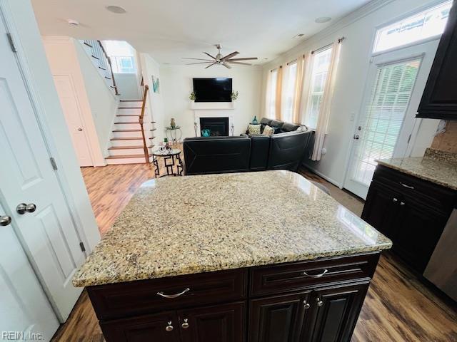 kitchen with ceiling fan, a kitchen island, a fireplace, light stone countertops, and a wealth of natural light