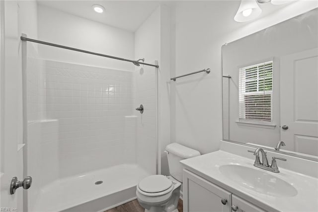 bathroom featuring vanity, wood finished floors, toilet, and tiled shower