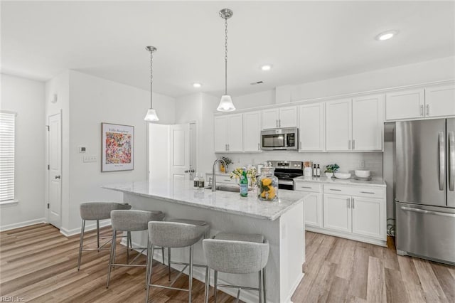 kitchen with light wood finished floors, appliances with stainless steel finishes, a breakfast bar area, and white cabinets