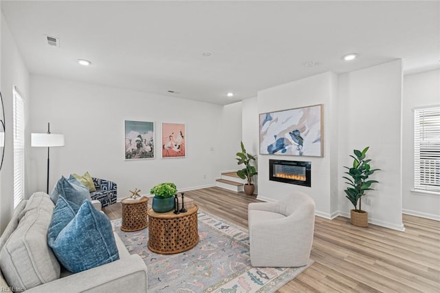living room featuring visible vents, recessed lighting, light wood-style flooring, and a glass covered fireplace