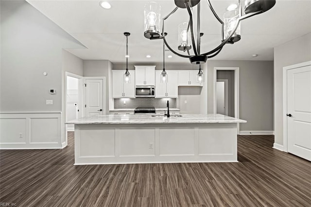 kitchen with appliances with stainless steel finishes, a large island with sink, white cabinets, backsplash, and dark wood-type flooring