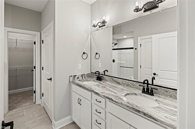 full bathroom with a spacious closet, a stall shower, double vanity, and a sink