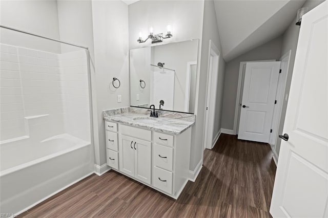 bathroom with wood finished floors,  shower combination, vanity, baseboards, and lofted ceiling